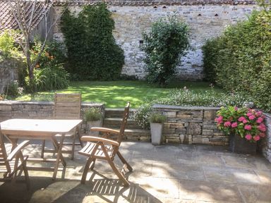 A patio with wooden chairs and table overlooking a garden with grass and plants at Willow Barn in Shapwick