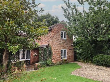 A brick house with white windows surrounded by trees and a garden with grass and gravel at The Coach House Apartment in Bredon