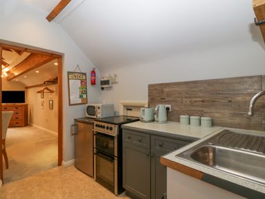 A kitchen with a stove refrigerator microwave kettle toaster and sink next to a living area with a television and dresser at The Coach House Apartment in Bredon
