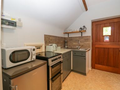 A kitchen with a microwave on a fridge next to an oven a sink with a faucet wooden door and shelves with glasses at The Coach House Apartment in Bredon