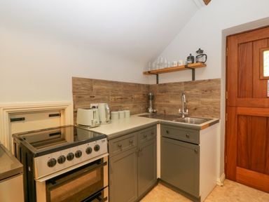 A kitchen corner with stove sink toaster kettle utensils and wooden shelf with cups and glasses at The Coach House Apartment in Bredon