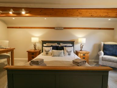 A bedroom with a bed flanked by two bedside tables and lamps next to an armchair at The Coach House Apartment in Bredon