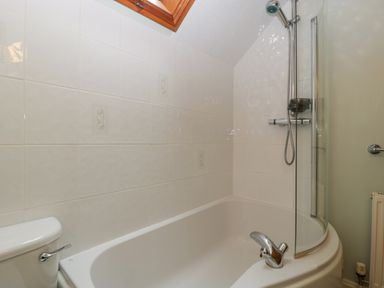 A bathroom with a white bathtub shower combination a toilet with a handle and a glass shower screen at The Coach House Apartment in Bredon
