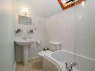 A bathroom with a pedestal sink, toilet, bathtub, wall mirror, and skylight window at The Coach House Apartment in Bredon