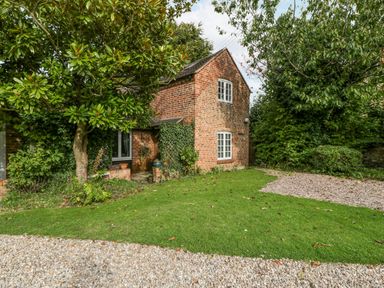 A brick house with white framed windows surrounded by trees and a green lawn at The Coach House Apartment in Bredon