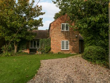 A brick house with white framed windows surrounded by trees grass and a gravel driveway at The Coach House Apartment in Bredon