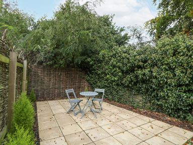A small outdoor patio with two chairs and a round table surrounded by leafy green bushes and wooden fencing at The Coach House Apartment in Bredon