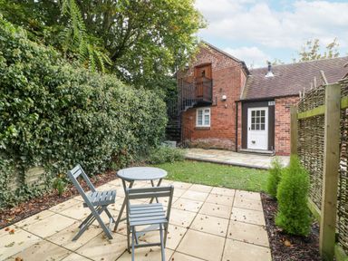 A patio with table and chairs and a garden area outside a brick house with spiral stairs at The Coach House Apartment in Bredon