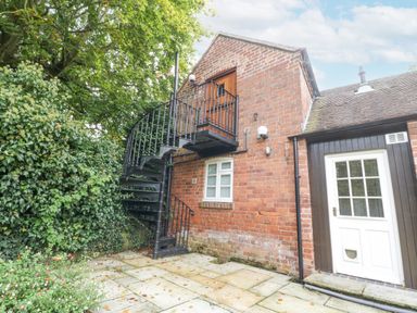 An outdoor patio area with a brick wall and a black spiral staircase leading to a wooden door above at The Coach House Apartment in Bredon