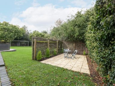 A garden with a small patio area with two chairs and a table near woven wooden fences and greenery at The Coach House Apartment in Bredon