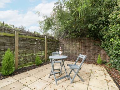 An outdoor patio with a small round table and two chairs near a woven wooden fence and greenery at The Coach House Apartment in Bredon