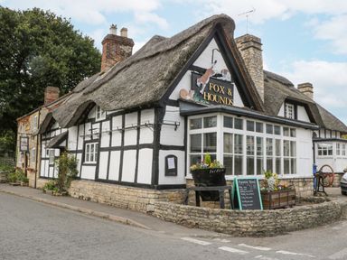 A thatched roof building with black and white timber framing and a sign reading Fox and Hounds at The Coach House Apartment in Bredon