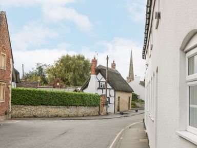 A street with various houses including a thatched roof cottage and a church spire in the background at The Coach House Apartment in Bredon