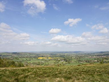 A wide view of green fields and scattered houses under a blue sky with clouds at The Coach House Apartment in Bredon