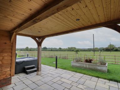 A covered patio with a hot tub and a planter overlooking a fenced grassy field at Hallgarth Farm Holiday Lodge in Peopleton