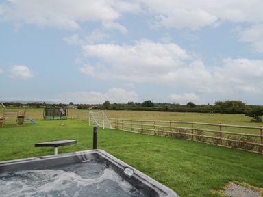 A backyard with a hot tub a small table a play structure a trampoline a soccer goal and fields at Hallgarth Farm Holiday Lodge in Peopleton