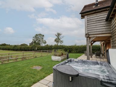 An outdoor area with a hot tub a wooden fence and a patio with tables and chairs at Hallgarth Farm Holiday Lodge in Peopleton