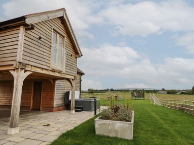 A wooden exterior building with a patio planter and children's play equipment in a fenced grassy yard at Hallgarth Farm Holiday Lodge in Peopleton