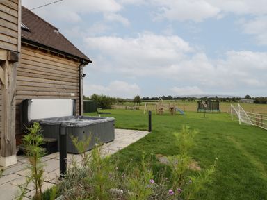 An outdoor area with a hot tub next to a wooden building and a playground with a slide trampoline and soccer goals at Hallgarth Farm Holiday Lodge in Peopleton