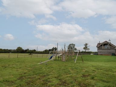 An outdoor playground with wooden climbing structures and a slide on a grassy field near a wooden building at Hallgarth Farm Holiday Lodge in Peopleton