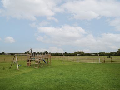 A grassy outdoor play area with a wooden climbing frame with swings slide and rope ladder and a soccer goal with a basketball hoop at Hallgarth Farm Holiday Lodge in Peopleton