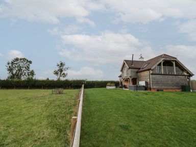 A wooden house with a fenced grassy yard and trees in the background at Hallgarth Farm Holiday Lodge in Peopleton