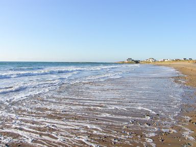 A beach with waves coming to shore and houses in the distance at Sgubor in Valley