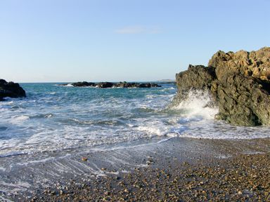 A rocky coastline with waves crashing against rocks and pebbles on the shore at Sgubor in Valley