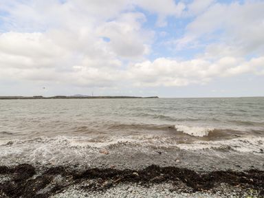 A rocky shoreline with seaweed and waves under a cloudy sky at Sgubor in Valley