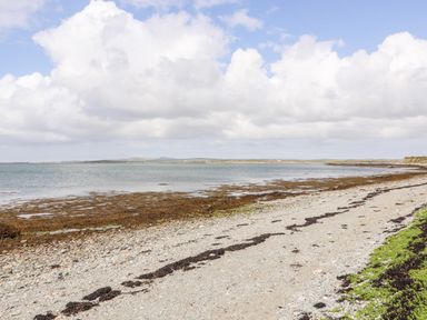 A rocky beach with seaweed near calm water and a cloudy sky at Sgubor in Valley