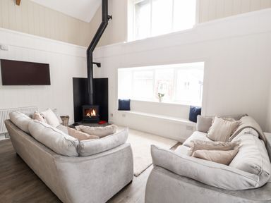A living room with two sofas a wood burning stove and a window seat with cushions at Sgubor in Valley