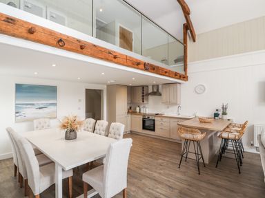 A kitchen and dining area with a white table and chairs and a wooden countertop with stools at Sgubor in Valley