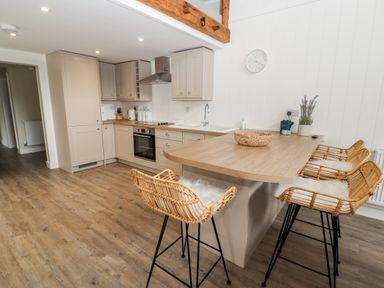 A kitchen with wooden floor cabinets an island with wicker bar stools and appliances at Sgubor in Valley