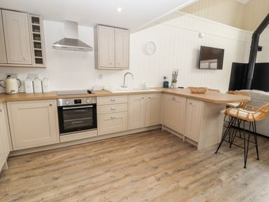 A kitchen with beige cabinets wooden countertops bar stools a wall clock and a mounted television at Sgubor in Valley