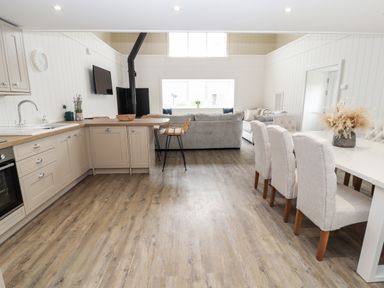 An open plan kitchen and living area with beige cabinets a dining table with chairs and a gray sofa at Sgubor in Valley