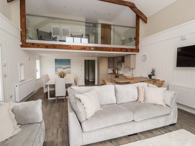 An open living room with sofas dining table kitchen and a mezzanine with armchairs at Sgubor in Valley