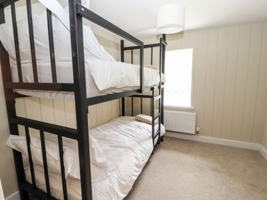 A bedroom with a black metal bunk bed white bedding a window and a radiator at Sgubor in Valley