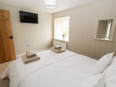 A bedroom with bed folded towels mounted TV and window with flower pot at Sgubor in Valley