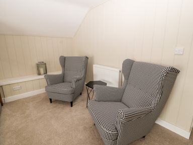 Two patterned armchairs and a small black side table in a beige carpeted room at Sgubor in Valley