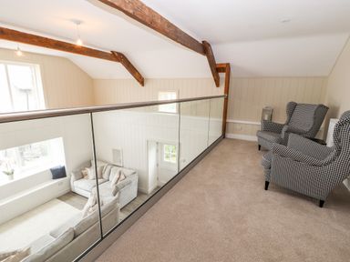 An upstairs area with two checkered armchairs and a glass railing overlooking a living room with sofas at Sgubor in Valley
