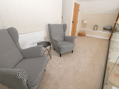 A sitting area with two patterned armchairs a small black side table a wooden door and carpeted floor at Sgubor in Valley