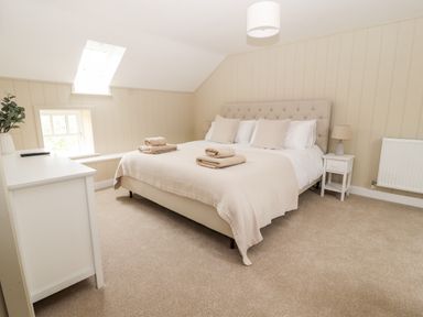 A bedroom with a bed with pillows and folded towels bedside table with a lamp and a white dresser with a plant at Sgubor Valley