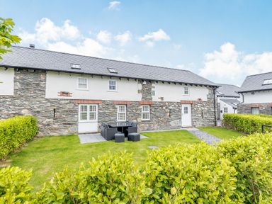 A stone and white exterior house with green lawn outdoor seating and hedges at Sgubor in Valley