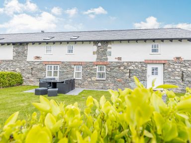 A stone and white exterior house with a patio dining set on a grass lawn at Sgubor in Valley