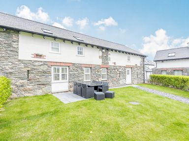 A stone and white exterior house with a patio and outdoor dining set on a grassy lawn at Sgubor in Valley