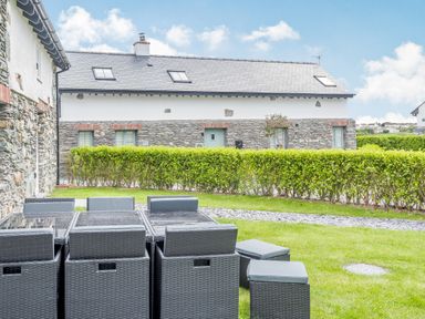 An outdoor patio area with black wicker furniture and a stone building with green bushes and a grassy lawn at Sgubor in Valley
