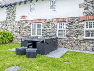 A stone and white wall exterior with windows and a black outdoor dining table set on a patio at Sgubor in Valley