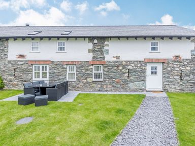 A stone house with white upper walls a white door and six windows a black outdoor dining set on a patio and a stone pathway in the grass at Sgubor in Valley