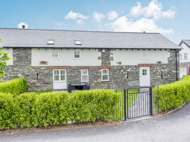 A stone and white cottage with a black metal gate and green hedges at Sgubor in Valley