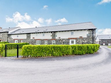 A stone and white house with multiple windows behind a green hedge and a gated entrance at Sgubor in Valley